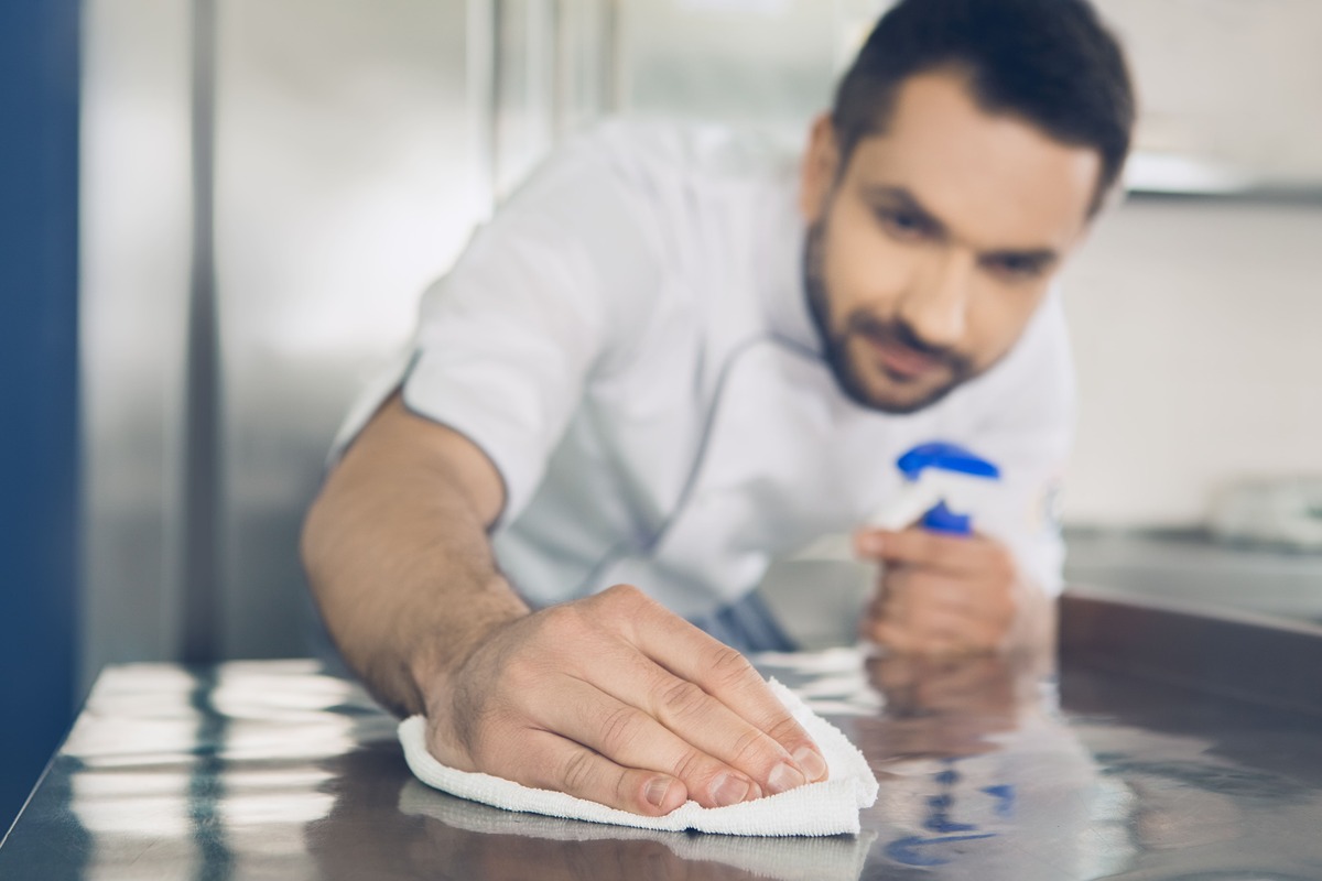 bucatar igienizeaza suprafata inox in bucatarie profesionala